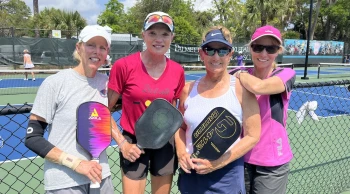 four women pickleball players holding their paddles posing on the court
